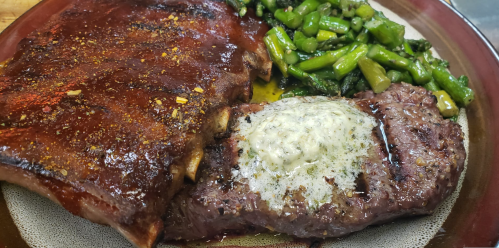 A plate featuring glazed ribs, a butter-topped steak, and sautéed asparagus.