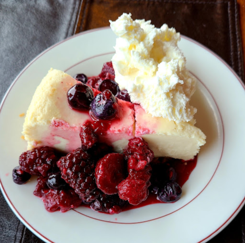 A slice of cheesecake topped with mixed berries and whipped cream on a white plate.