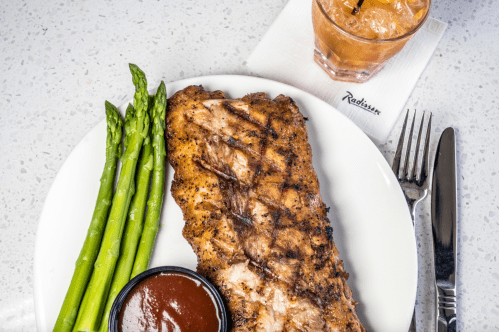 Grilled fish fillet with asparagus and dipping sauce, served with a cocktail on a white plate.