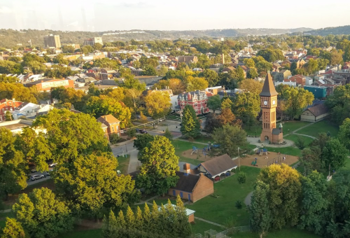 Aerial view of a park with a clock tower, surrounded by trees and buildings in a small town.