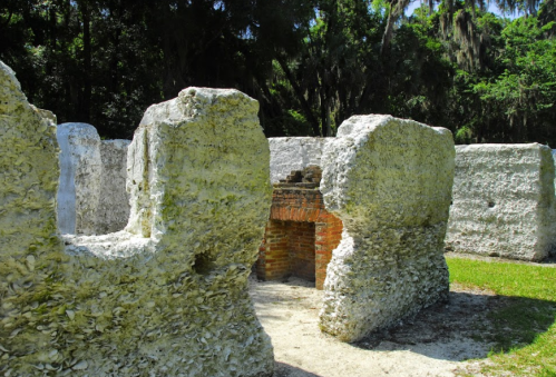 Ruins of a stone structure surrounded by greenery, with moss-covered walls and a brick fireplace visible.