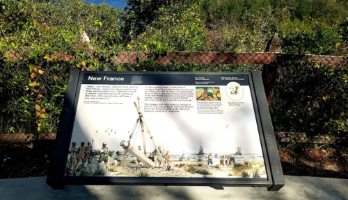 A historical sign about New France, featuring illustrations and text, set against a lush green background.