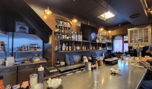 A cozy bar with a variety of liquor bottles, a stainless steel counter, and warm lighting.