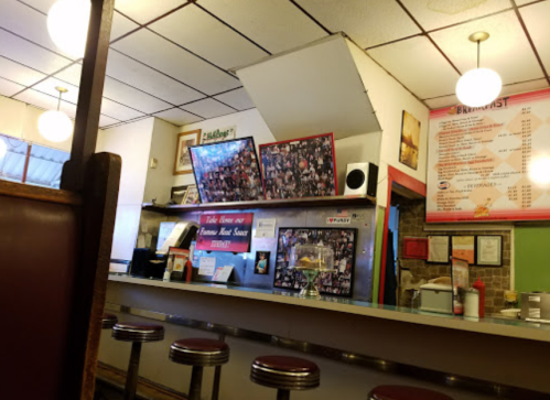 A cozy diner interior with a counter, stools, and a wall covered in photos, featuring a menu board and warm lighting.