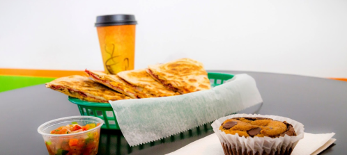A basket of quesadillas with salsa, a coffee cup, and a chocolate chip muffin on a table.