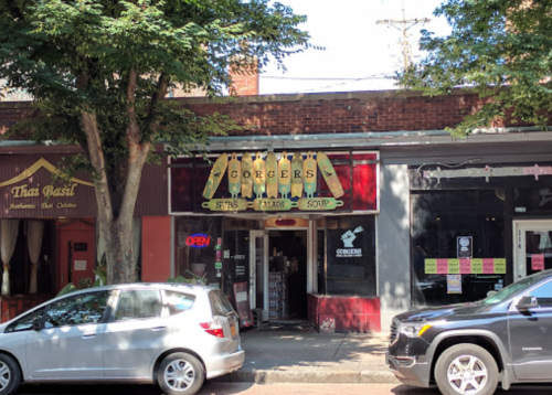 A storefront with a sign reading "Gorgers" and an open sign, surrounded by trees and parked cars.