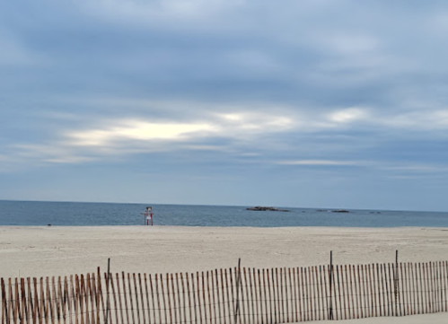 A serene beach scene with a sandy shore, gentle waves, and a lifeguard tower in the distance under a cloudy sky.