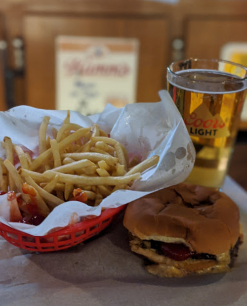 A basket of fries with ketchup, a burger, and a glass of beer on a table.