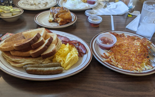 A breakfast plate with toast, eggs, bacon, sausage, and hash browns, accompanied by condiments and drinks.