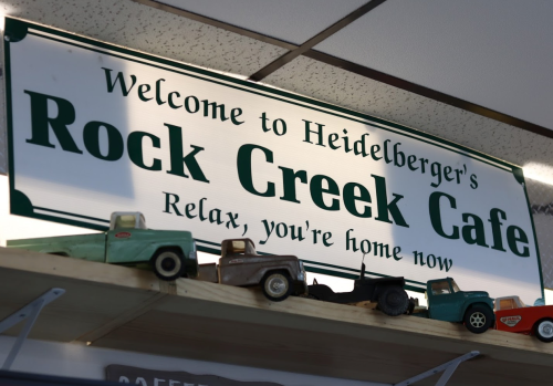 Sign for Rock Creek Cafe with vintage toy trucks displayed below. Text reads: "Welcome to Heidelberger's Rock Creek Cafe."