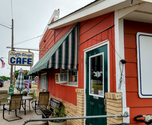A red cafe building with green awnings, outdoor seating, and a sign reading "Cafe" in a small town setting.