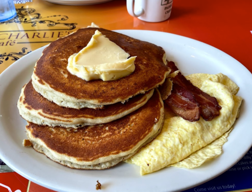 A plate of three fluffy pancakes topped with butter, alongside a bacon-filled omelet.
