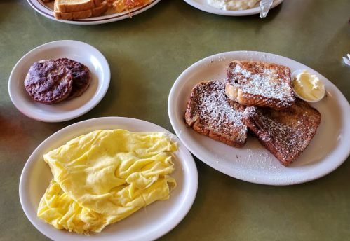 A plate with French toast dusted with powdered sugar and butter, alongside a side of scrambled eggs and sausage patties.
