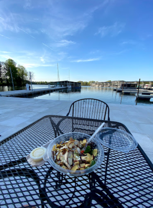 A salad on a table by the water, with a clear blue sky and boats in the background.