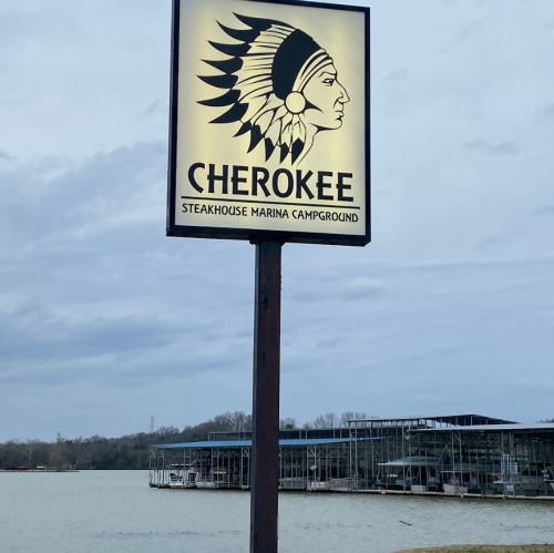 Sign for Cherokee Steakhouse Marina Campground featuring a Native American profile, with a lake and marina in the background.