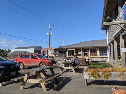 A sunny outdoor area with picnic tables, a red SUV parked nearby, and a building with large windows in the background.