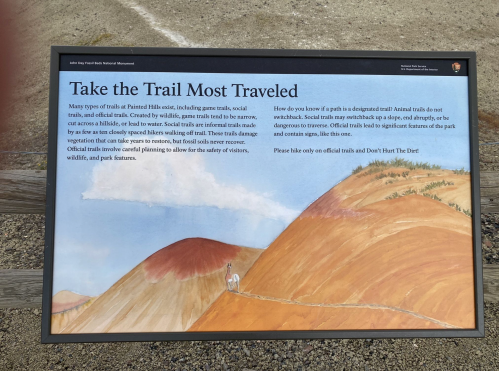 Sign explaining trail types and safety in a national park, with a colorful landscape in the background.