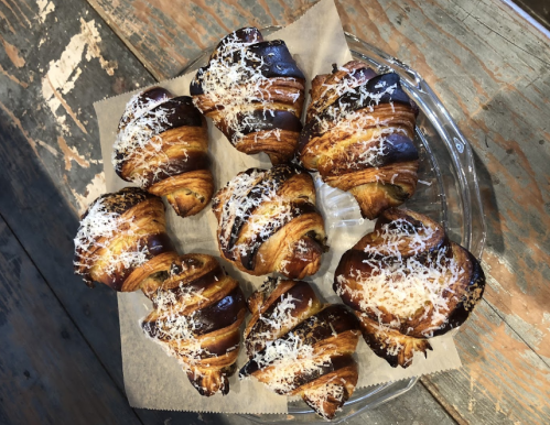 A plate of freshly baked croissants topped with a sprinkle of cheese, arranged on a rustic wooden table.