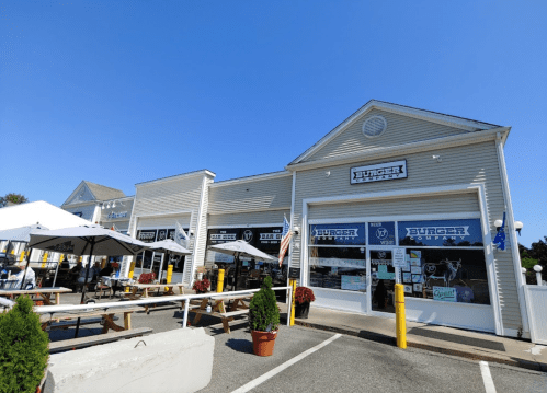 Exterior of a burger restaurant with outdoor seating, flags, and a clear blue sky.