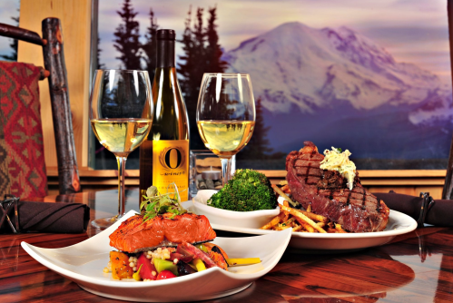 A beautifully arranged table with gourmet dishes, wine, and a stunning mountain view in the background.