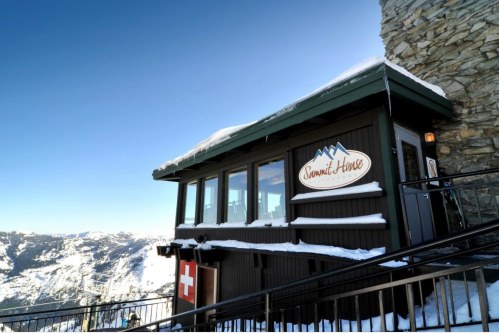 A cozy mountain lodge with a sign reading "Summit House," surrounded by snow and scenic views.