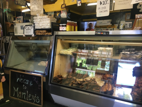 Interior of a market with a display case of meats and a chalkboard sign welcoming customers to Manley's.