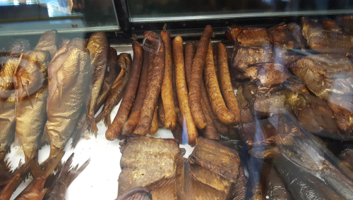 A display of various smoked fish and sausages in a glass case.