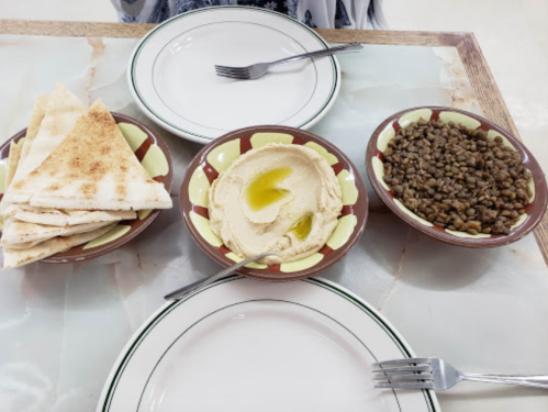 A table setting with pita bread, hummus, and lentils in bowls, alongside empty plates and forks.