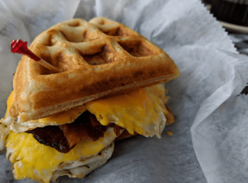 A waffle sandwich filled with bacon, melted cheese, and a fried egg, secured with a toothpick.