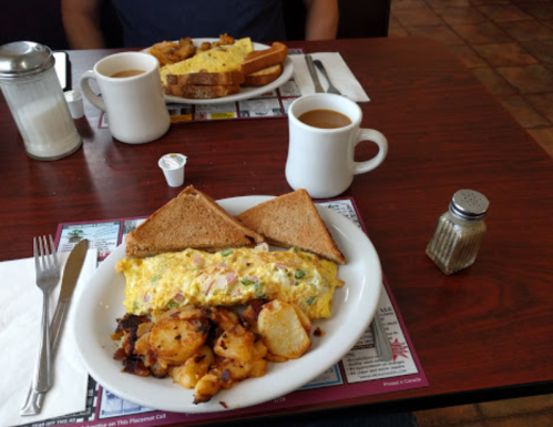 A hearty breakfast with an omelette, hash browns, toast, coffee, and cream on a table in a diner setting.