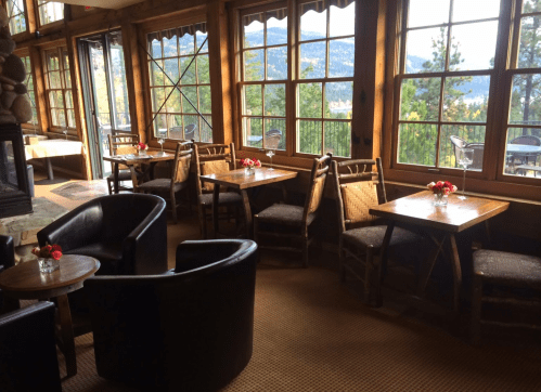 Cozy dining area with wooden tables, chairs, and large windows showcasing a mountain view.