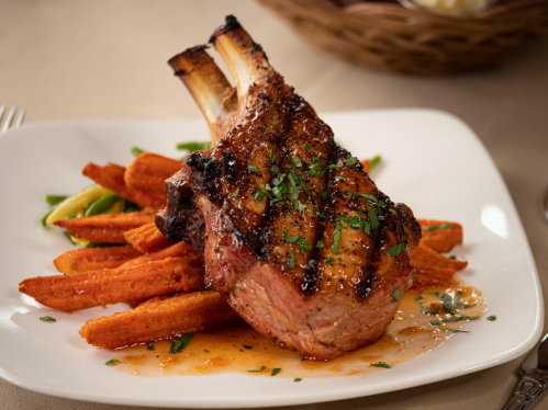 Grilled pork chop on a plate with sweet potato fries, garnished with herbs and a drizzle of sauce.