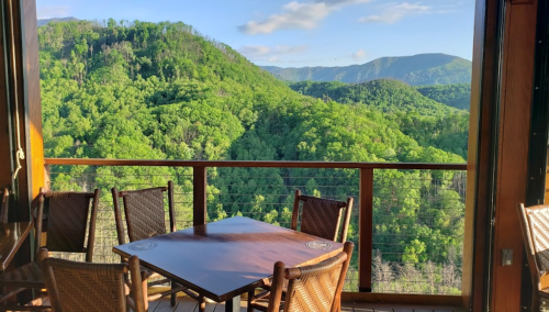 A scenic view of lush green mountains from a balcony with a wooden table and chairs.