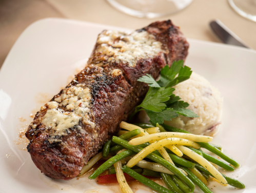 A plate featuring a grilled steak topped with cheese, served with mashed potatoes and mixed green beans.