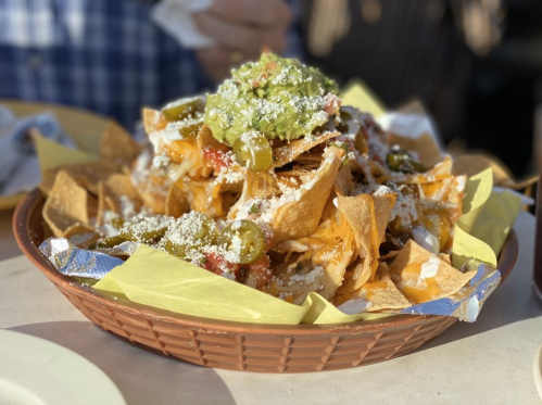 A large plate of nachos topped with cheese, guacamole, jalapeños, and sour cream, served in a woven basket.
