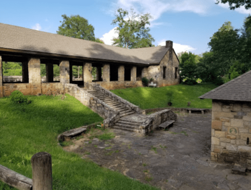 A stone building with a sloped roof, surrounded by greenery and steps leading to a patio area.