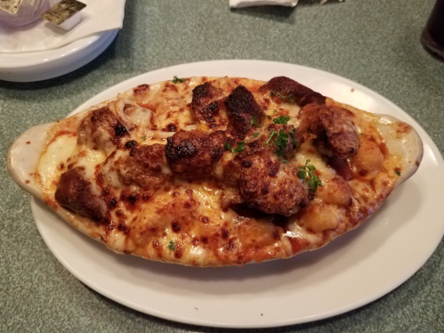 A baked dish with melted cheese, meatballs, and herbs, served in a white oval dish on a green table.