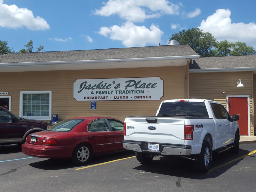 Exterior of Jackie’s Place restaurant with a sign reading "Breakfast, Lunch, Dinner" and parked cars in front.