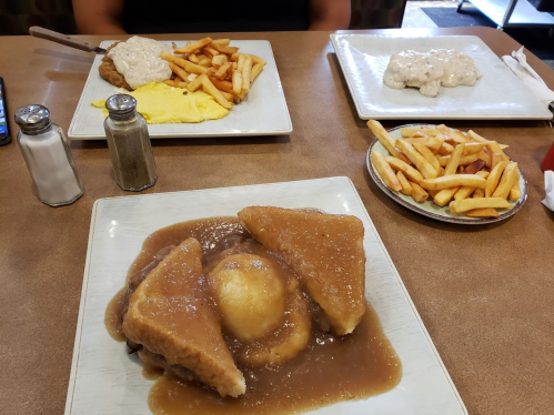 A table with two plates of food: one with fried chicken, fries, and eggs, and another with biscuits and gravy.