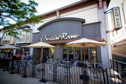 Exterior of The Sardine Room restaurant with outdoor seating and umbrellas on a sunny day.