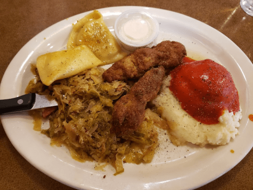 A plate of food featuring fried chicken strips, mashed potatoes with sauce, cabbage, and dumplings.