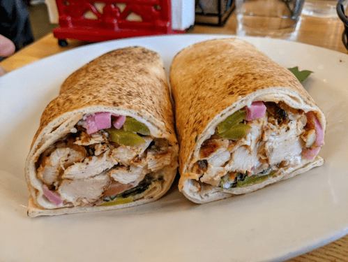 Two grilled chicken wraps filled with vegetables, sliced and served on a white plate.