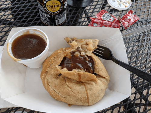 A savory pastry filled with meat and gravy, served with a side of sauce and condiments on a black table.