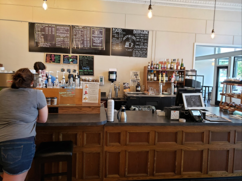 A coffee shop counter with a menu board, drinks, and pastries; a customer is ordering at the counter.