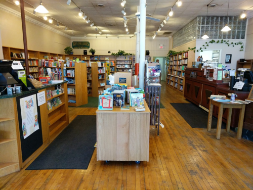A cozy bookstore interior with wooden shelves, a central display table, and warm lighting.