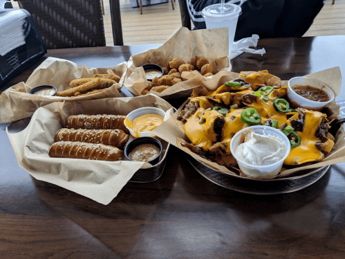 A table with two plates of food: loaded nachos with cheese and jalapeños, and a platter of fried snacks with dipping sauces.