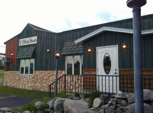 Exterior of a rustic steakhouse with a stone foundation, wooden siding, and a welcoming entrance.
