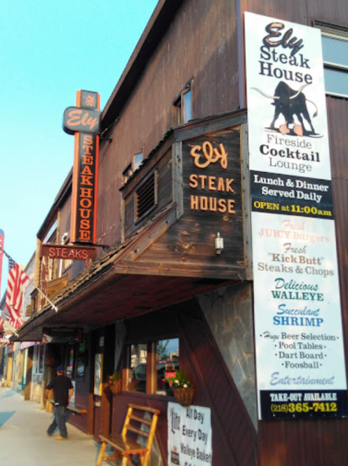Exterior of Ely Steak House with signs for dining options, including steaks, shrimp, and a cocktail lounge.