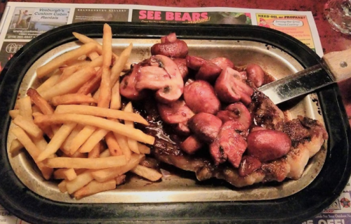 A plate of grilled steak topped with mushrooms, served with a side of golden French fries.