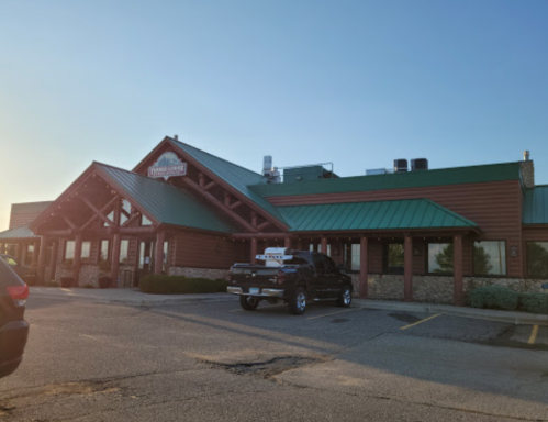 A rustic restaurant with a green metal roof and wooden accents, featuring a parking lot and a black truck in front.